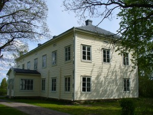 Puurakenteinen kaksikerroksinen vanha pappila, jossa on ulkoneva porstua. Vaalea väritys ja ruutuikkunat. Ympärillä puita.