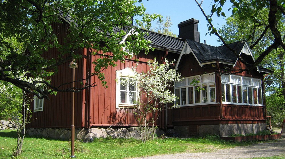 vanha punamultamaalattu talo, valkoiset ikkunanpuitteet, kuvattu alkukesällä, ikkunan edessä pieni kukkiva puu